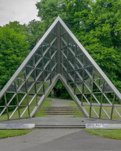 Dreiecke durchlässige Stahlskulptur bestehend aus Einzelprofilen mit Glaselementen, installiert in einem Park.