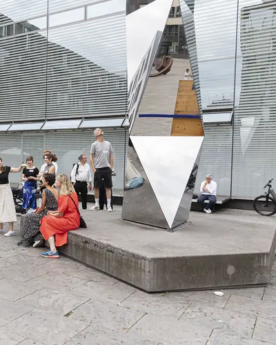 spiegelnde Polylit Skulptur von Karsten Nicolai auf dem Kleinen Schlossplatz im Vordergrund umgeben von mehreren Menschen während einer Führung